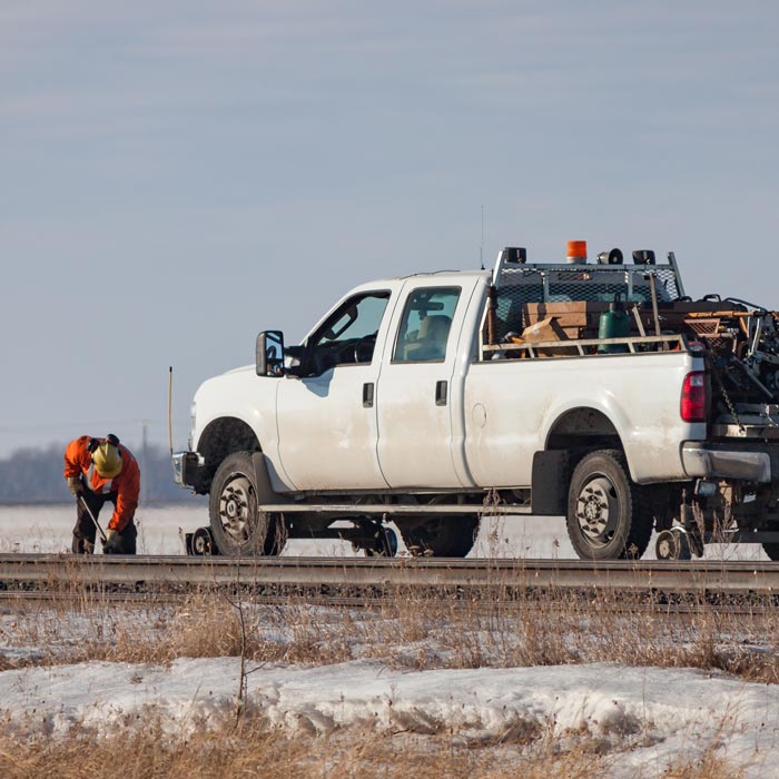 A rail worker is working on track beside a white pickup rail truck